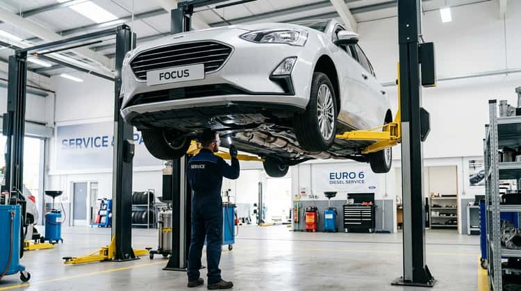Ein Ford Focus mit Dieselmotor auf einer Hebebühne in einer Werkstatt, ein Mechaniker inspiziert die Abgasanlage