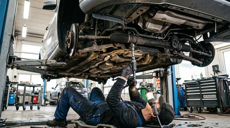 Ein Mechaniker in einer Werkstatt arbeitet an der Lenkungsverschraubung eines Fahrzeugs, um eine Befestigungsschraube auszutauschen
