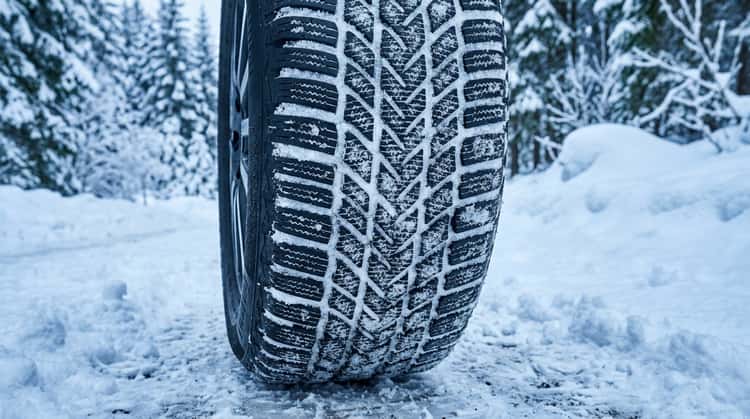 Nahaufnahme eines Winterreifens mit feinem Schneeprofil auf schneebedecktem Untergrund
